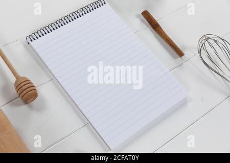 View of a composition with a notebook with wooden spoon and whisker on white wooden surface Stock Photo