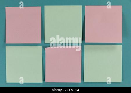 View of six green and pink sheets of paper in one size on plain blue background Stock Photo