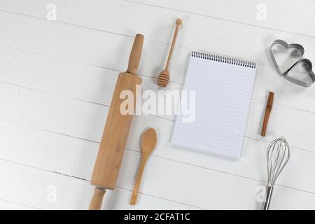 View of a composition of a notebook with cookie cutters, whisker and rolling pin on white surface Stock Photo