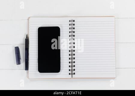 View of a black smartphone, a notebook and a black pen on plain white background Stock Photo