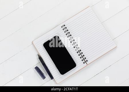 View of a black smartphone, a notebook and a black pen on plain white background Stock Photo