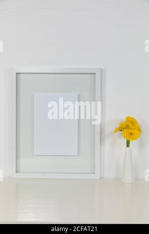 View of a picture frame, with yellow tulips placed in a glass vase on plain white background Stock Photo