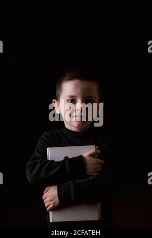 Adorable serious child in casual wear holding tablet in hands and looking at camera with determined look isolated on black background Stock Photo