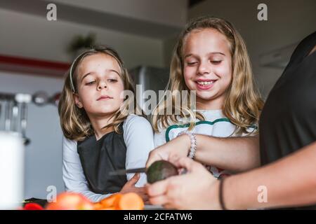 anonymous adult showing little girls to cook healthy salad in kitchen together Stock Photo