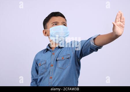 Indian cute young boy wearing surgical mask saying no or stop by hand gesture Stock Photo