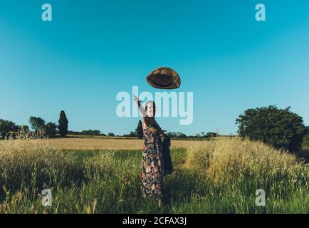 Side view of excited farmer Woman tossing straw hat up looking at camera in a grass meadow on a sunny afternoon Stock Photo
