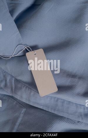 Clothing paper tag on ligh blue fabric. Fashion brand name mock up, closeup, top view, copy space for text Stock Photo