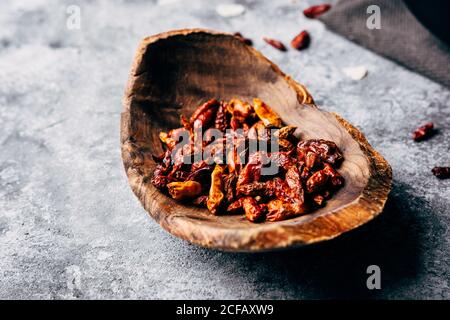 From above of boat shaped wooden plate with sun dried tomatoes and chili peppers on shabby gray table in kitchen Stock Photo