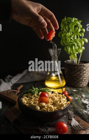 Man adding tomatoes to bowl with ravioli Stock Photo