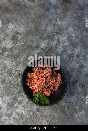 From above top view herbs on bowl with minced meat placed on gray table in kitchen Stock Photo