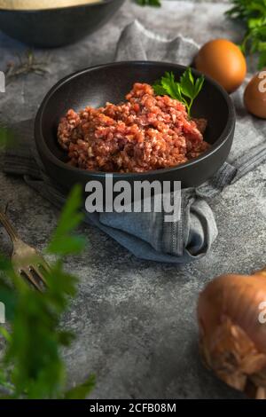 From above top view raw onions, eggs and herbs placed on gray table near bowl with minced meat salt in kitchen Stock Photo