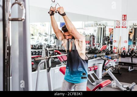 Powerful determined sportsman doing exercise with barbell at squat rack during weightlifting training with personal coach in modern gym Stock Photo
