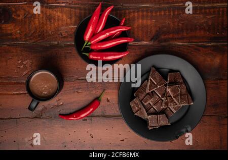 Mug of fresh hot drink placed on lumber tabletop near plate with pieces of chocolate and chili pepper Stock Photo