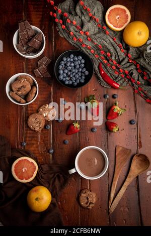 Mug of tasty hot chocolate placed on timber tabletop near assorted desserts and fruits for breakfast Stock Photo