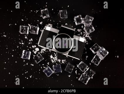 Top view of vintage photo camera surrounded by ice cubes showing concept of well preserved gadget on black background Stock Photo