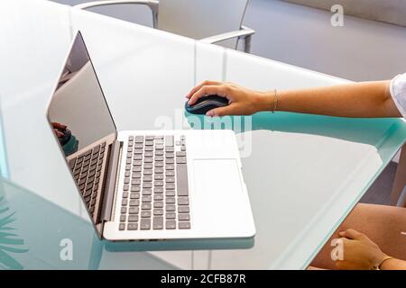 Overhead crop Woman sitting at glass table browsing laptop and using wireless mouse in office on daytime Stock Photo