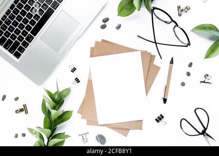 office desk workspace with paper blank, green leaves. Laptop, glasses on white background. Magazines, websites, social media. Flat lay, top view. Stock Photo