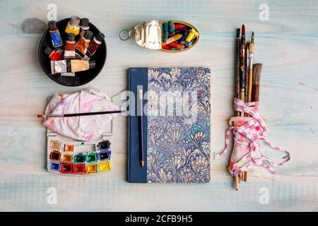Top view of creative sketchbook and paintbrushes arranged on table with watercolor and pastel colors Stock Photo