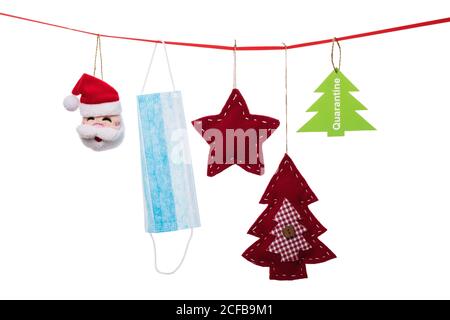 Christmas decorations and a medical mask hang on a decorative ribbon isolated on a white background. Quarantine concept Stock Photo