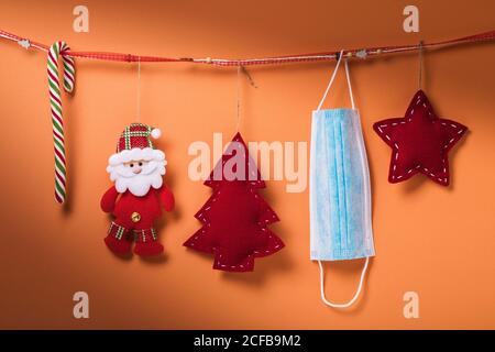 Christmas decorations and a medical mask hang on a decorative ribbon on a colored background. Quarantine concept for the new year Stock Photo