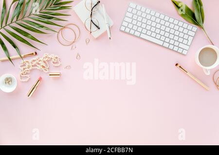 Office table desk with computer, green leaves palm, clipboard. Top view. Flat lay. Home office workspace. Women's accessories on pink background.  Stock Photo