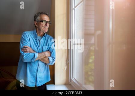 Senior man looking out of window at home Stock Photo