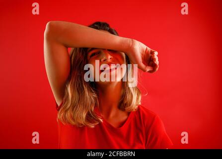 Happy young Woman smiling and looking at camera while standing against red background with arm over the head Stock Photo