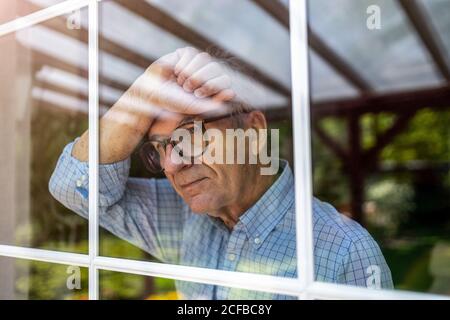 Senior man looking out of window at home Stock Photo
