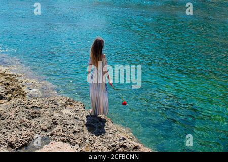 A woman from behind with a flower in her hand admires the sea Stock Photo