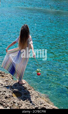 A woman from behind with a flower in her hand admires the sea Stock Photo