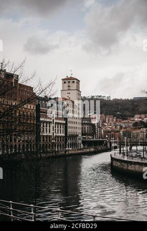 Gray clouds floating on sky over beautiful old buildings and canal with rippled water on dull day in Bilbao, Spain Stock Photo