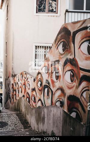 Shabby concrete fence decorated with many painted eyes on old street of Lisbon, Portugal Stock Photo