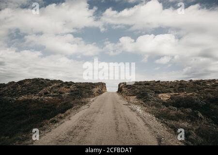 Beautiful white clouds floating on blue sky over rough hill with narrow countryside road Stock Photo