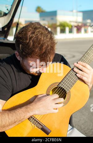 Close up portrait of young redhead man playing guitar in the street. Stock Photo