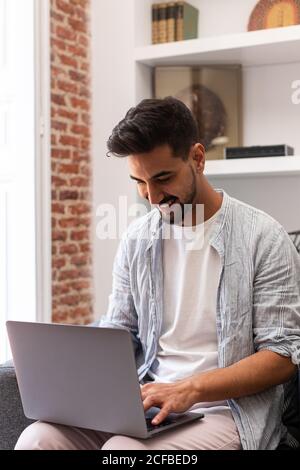 Bearded ethnic man using laptop while working on remote project at home Stock Photo