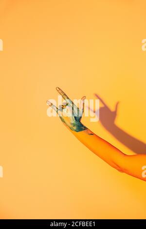 anonymous female with hand painted in blue color showing rock gesture on orange background in studio Stock Photo
