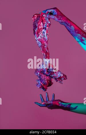 unrecognizable female with painted hands holding piece of aluminium crumpled foil on violet background in studio Stock Photo
