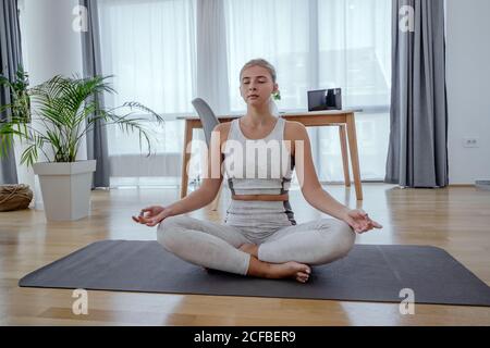 Beautiful active young woman meditating in yoga asana lotus pose at home. Healthy lifestyle and sports concept. Series of exercise poses. Stock Photo