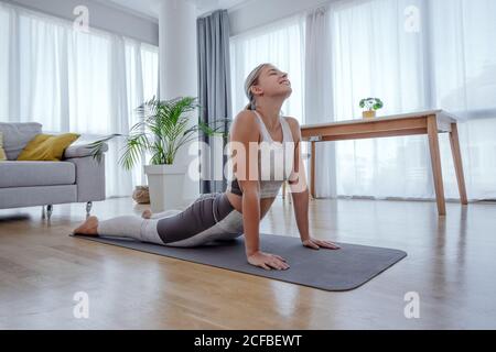 Beautiful active young woman practices yoga asana upward facing dog pose at home. Healthy lifestyle and sports concept. Series of exercise poses. Stock Photo