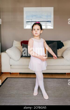 Cute girl in leotard and tights sitting on floor near sofa and putting on  dance shoes before ballet rehearsal at home Stock Photo - Alamy