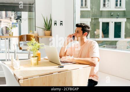 Crop man using laptop and talking phone in cafe Stock Photo