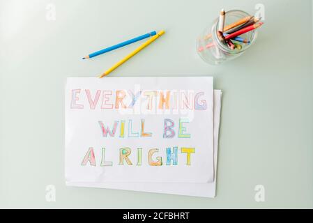Top view of composition with multicolored pencils in glass jar and colorful drawing on paper with positive inscription placed on white table Stock Photo