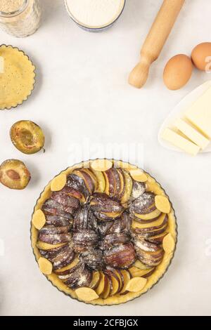Homemade pie with plums and sugar placed on the white background. Tart with raw plums. Top view, flat lay. Stock Photo