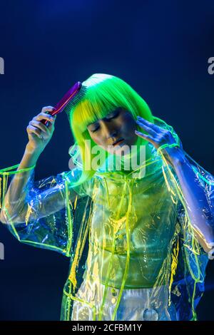 Young adorable Asian Woman in futuristic transparent plastic wear brushing yellow hair Stock Photo