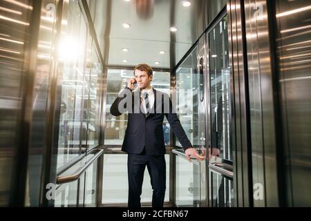 Portrait of cheerful men office worker talking on mobile phone while standing in elevator Stock Photo