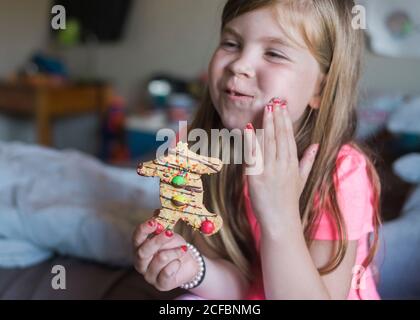 Young girl eating a gingerbread man in her bedroom Stock Photo