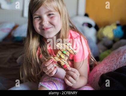 Young girl smiling and eating a gingerbread man in her bedroom Stock Photo