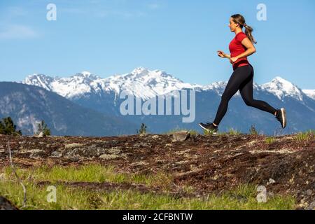 Side view of strong sportswoman running against snowy mountain ridge during fitness workout in countryside Stock Photo