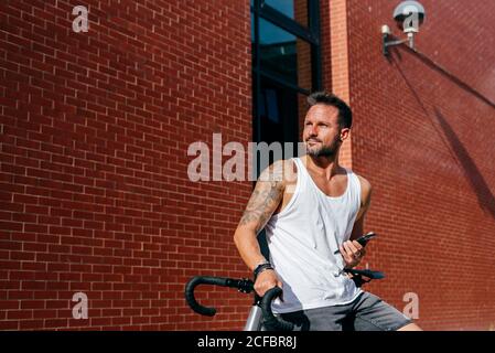 Handsome male cyclist in sportswear using smartphone while resting on bike next to red brick wall Stock Photo