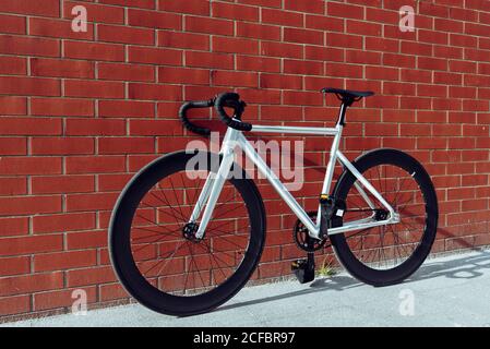 New modern white road bicycle with black handle bar parked against red brick wall Stock Photo